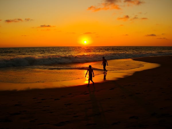 Dos siluetas caminan a la orilla del mar durante un vibrante atardecer naranja sobre el Pacífico