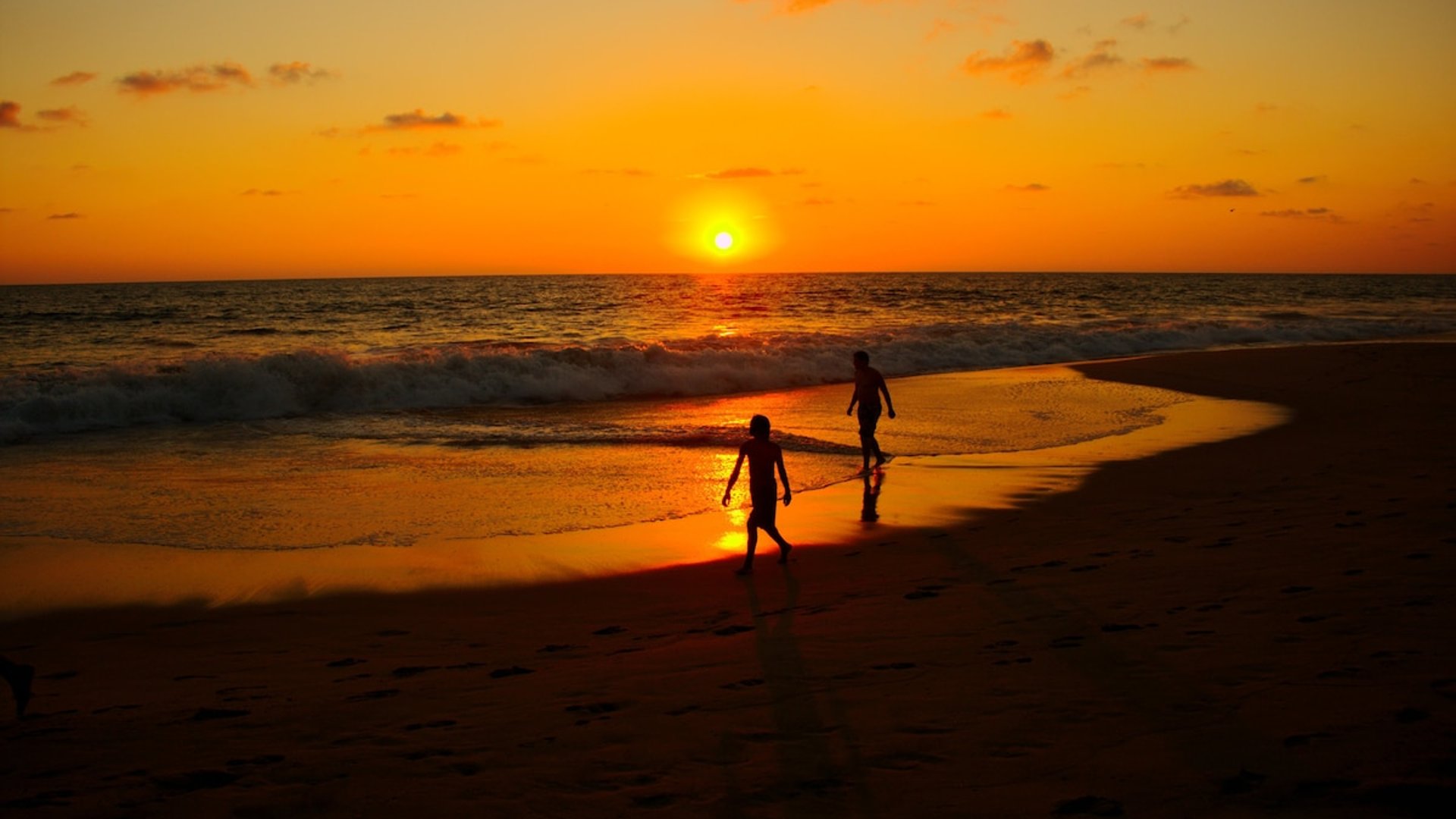 Dos siluetas caminan a la orilla del mar durante un vibrante atardecer naranja sobre el Pacífico