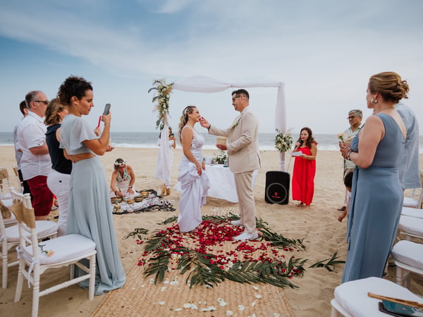 Ceremonia de boda en playa con arco floral blanco y pasillo de pétalos rojos frente al mar