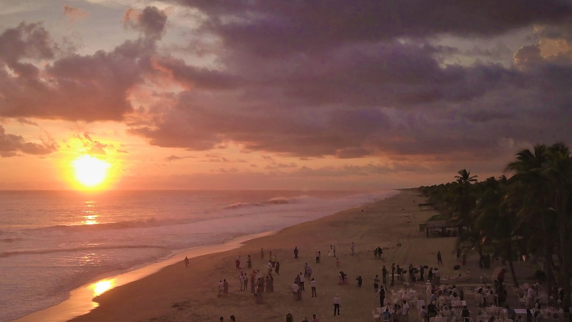 Banquete de bodas en la playa al atardecer con cielo dramático en tonos naranja y violeta sobre el Pacífico