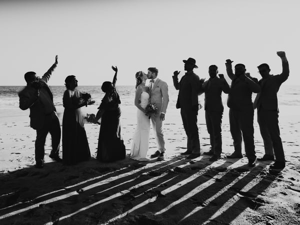Celebración de boda en playa con cortejo festivo frente al mar al atardecer