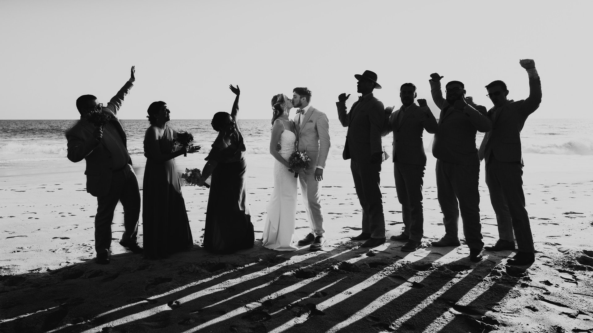 Celebración de boda en playa con cortejo festivo frente al mar al atardecer