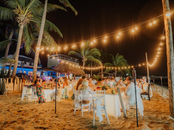 Recepción nocturna de boda en playa con mesas bajo luces colgantes y palmeras tropicales