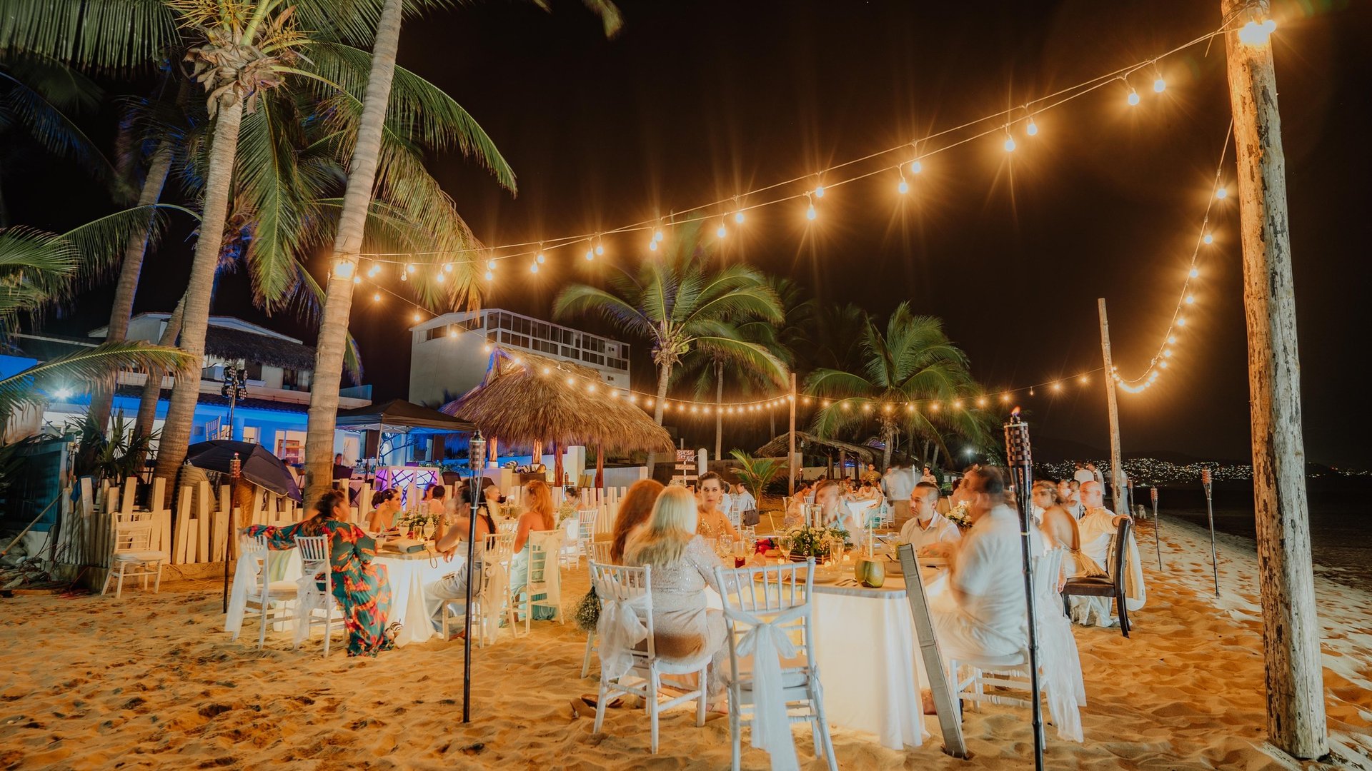 Recepción nocturna de boda en playa con mesas bajo luces colgantes y palmeras tropicales