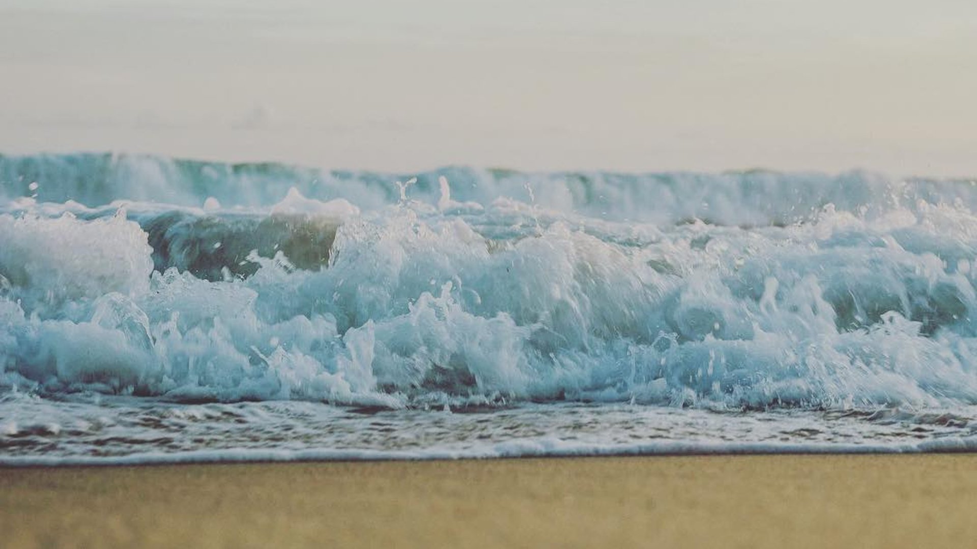 Olas turquesas rompiendo sobre la orilla de arena en la costa del Pacífico, atmósfera serena y luz difusa