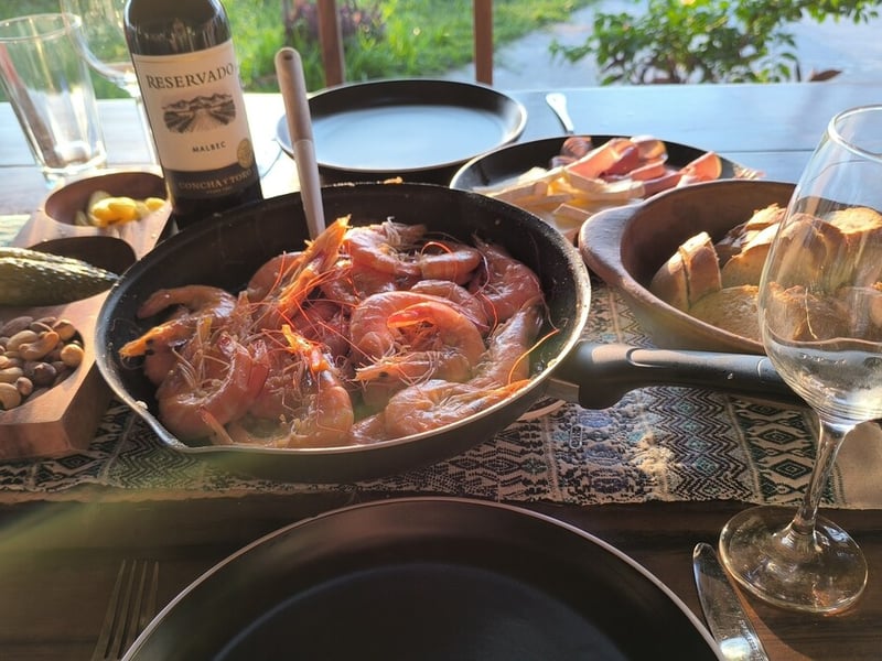 Garlic shrimp in a skillet with red wine and bread on an outdoor table