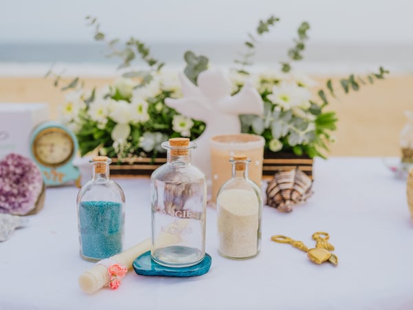 Mesa de ceremonia en playa con botellas de arena, flores blancas y vista al mar