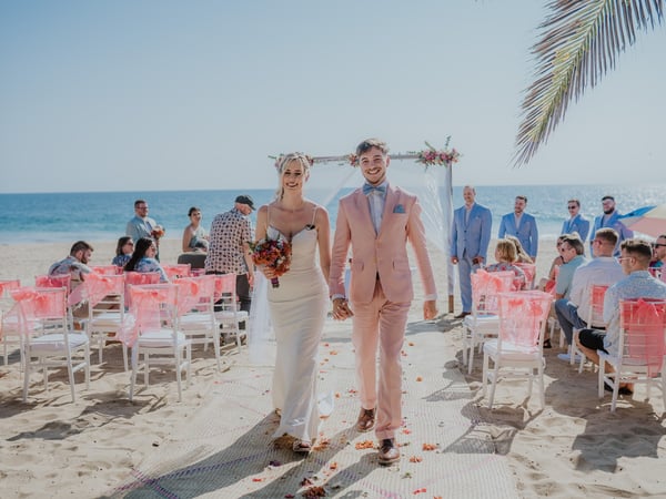 Ceremonia de boda en playa con sillas blancas decoradas, arco floral y vista al Pacífico