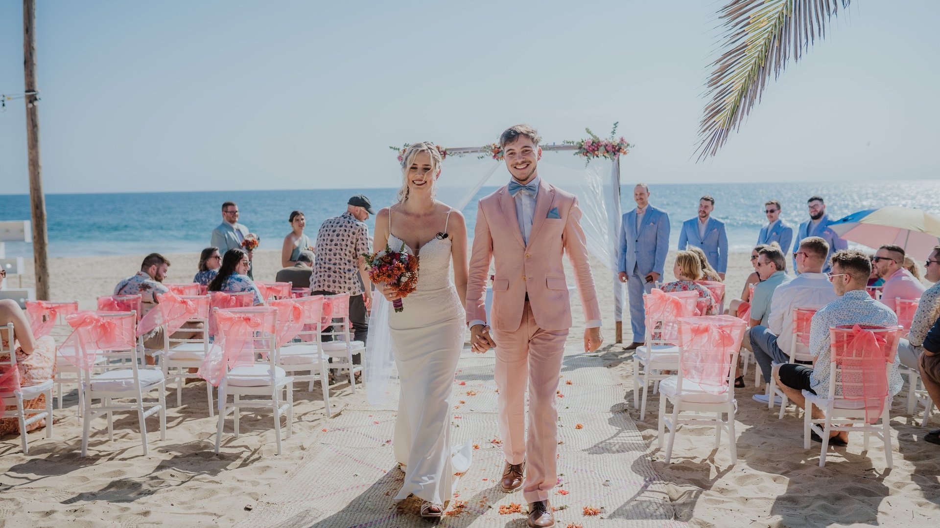 Ceremonia de boda en playa con sillas blancas decoradas, arco floral y vista al Pacífico
