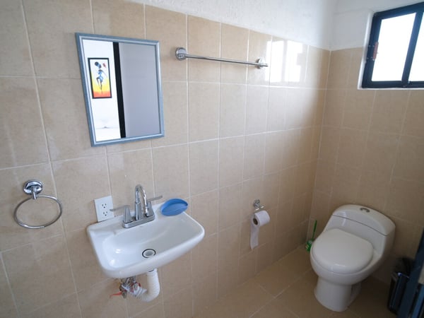 Baño sencillo con lavabo, espejo y sanitario, revestido de azulejo beige y accesorios cromados