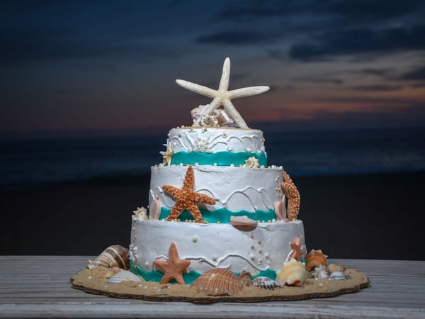 Pastel de bodas de tres pisos decorado con estrellas de mar y conchas frente al mar al atardecer