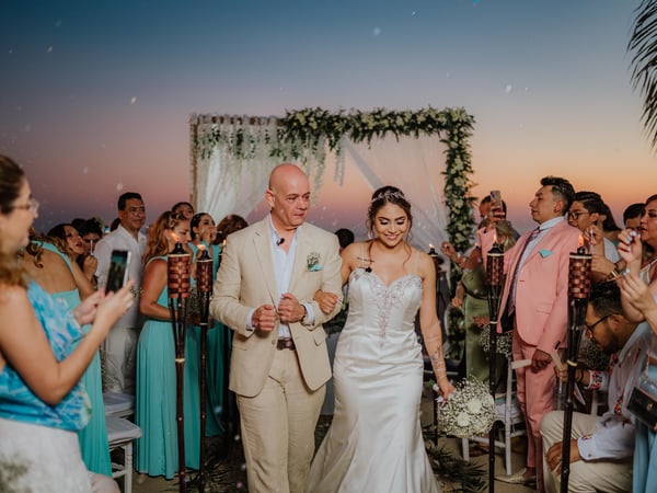 Ceremonia de boda al atardecer con arco floral decorado y vista al mar entre palmeras