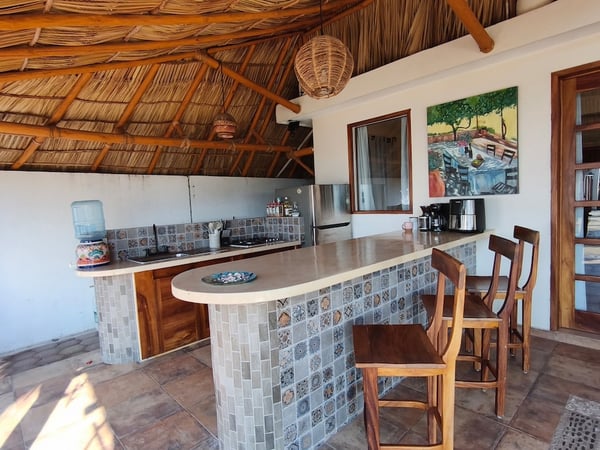 Cocina palapa con barra de mosaico talavera, sillas de madera y techo de palapa natural