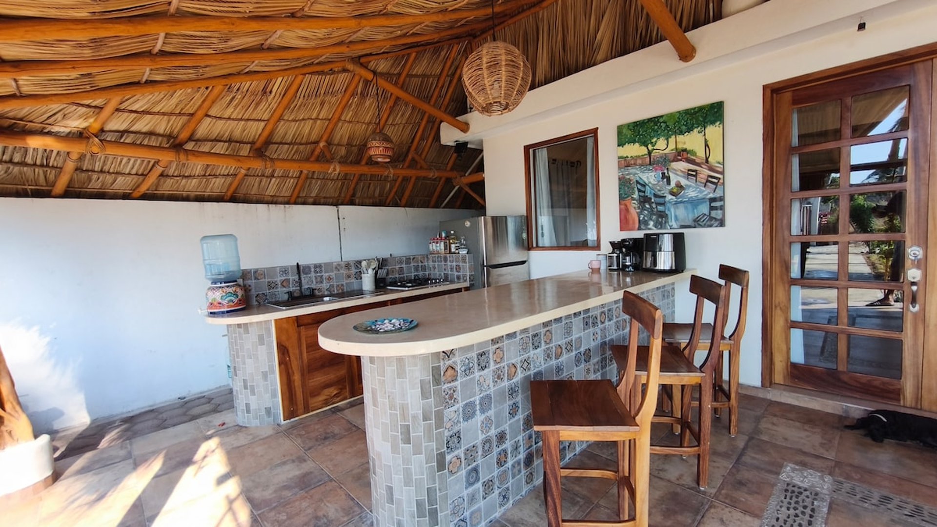 Cocina palapa con barra de mosaico talavera, sillas de madera y techo de palapa natural