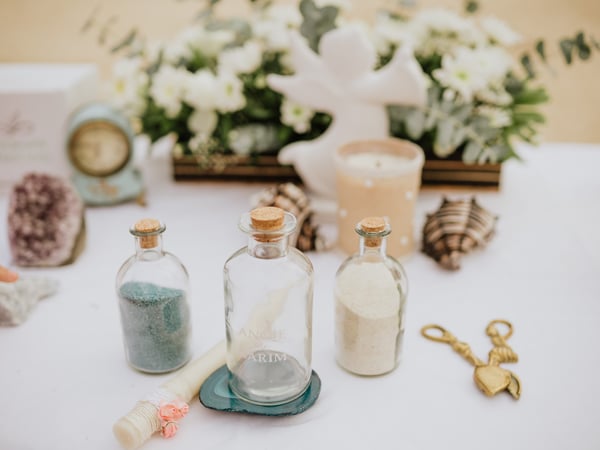 Mesa de ceremonia decorada con botellas de arena, flores blancas y conchas marinas