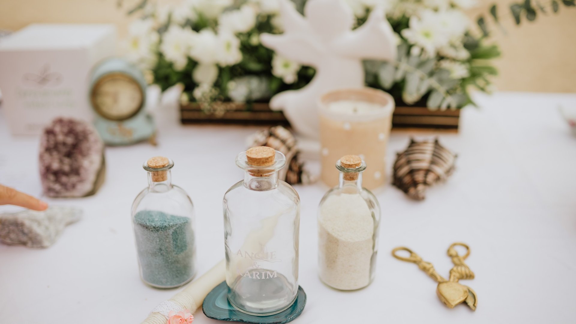 Mesa de ceremonia decorada con botellas de arena, flores blancas y conchas marinas