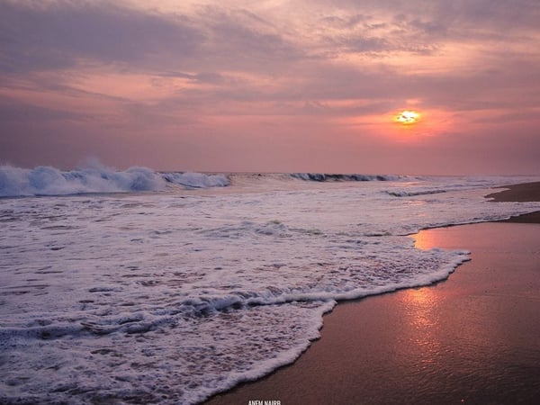 Oleaje intenso en la playa al atardecer con cielo rosado y reflejo del sol en la arena húmeda