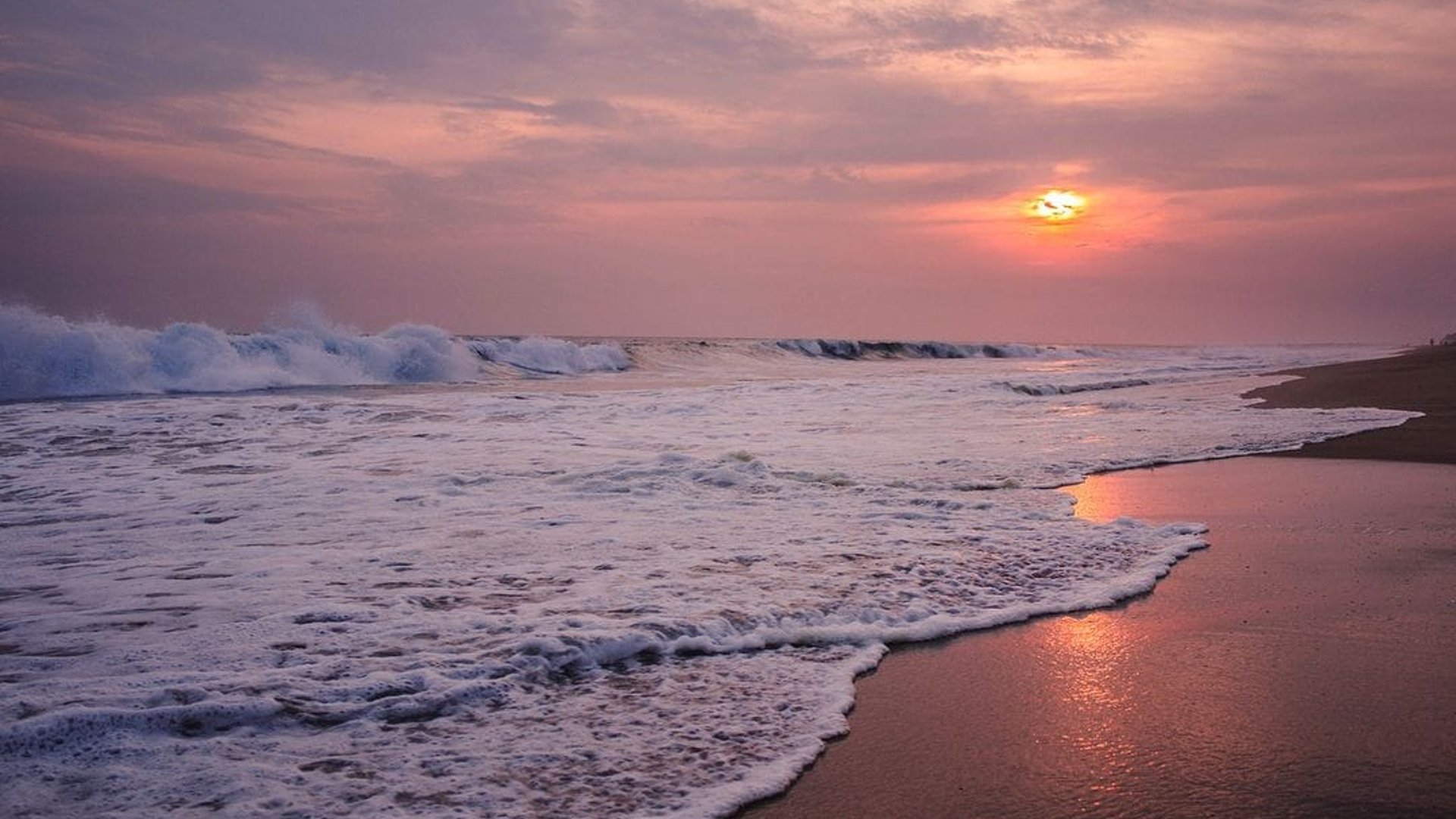 Oleaje intenso en la playa al atardecer con cielo rosado y reflejo del sol en la arena húmeda