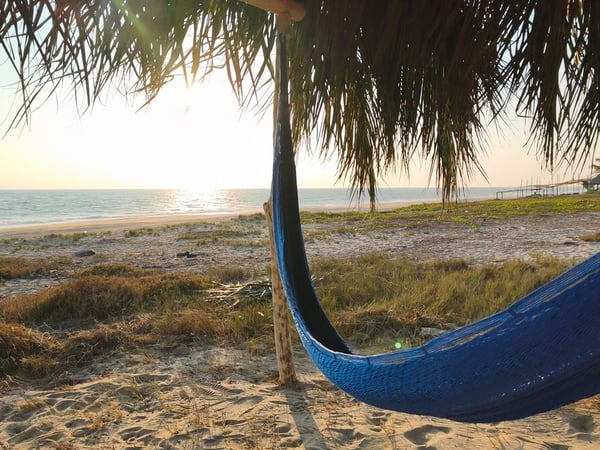 Hamaca azul bajo palapa frente al mar con luz dorada del atardecer en la playa