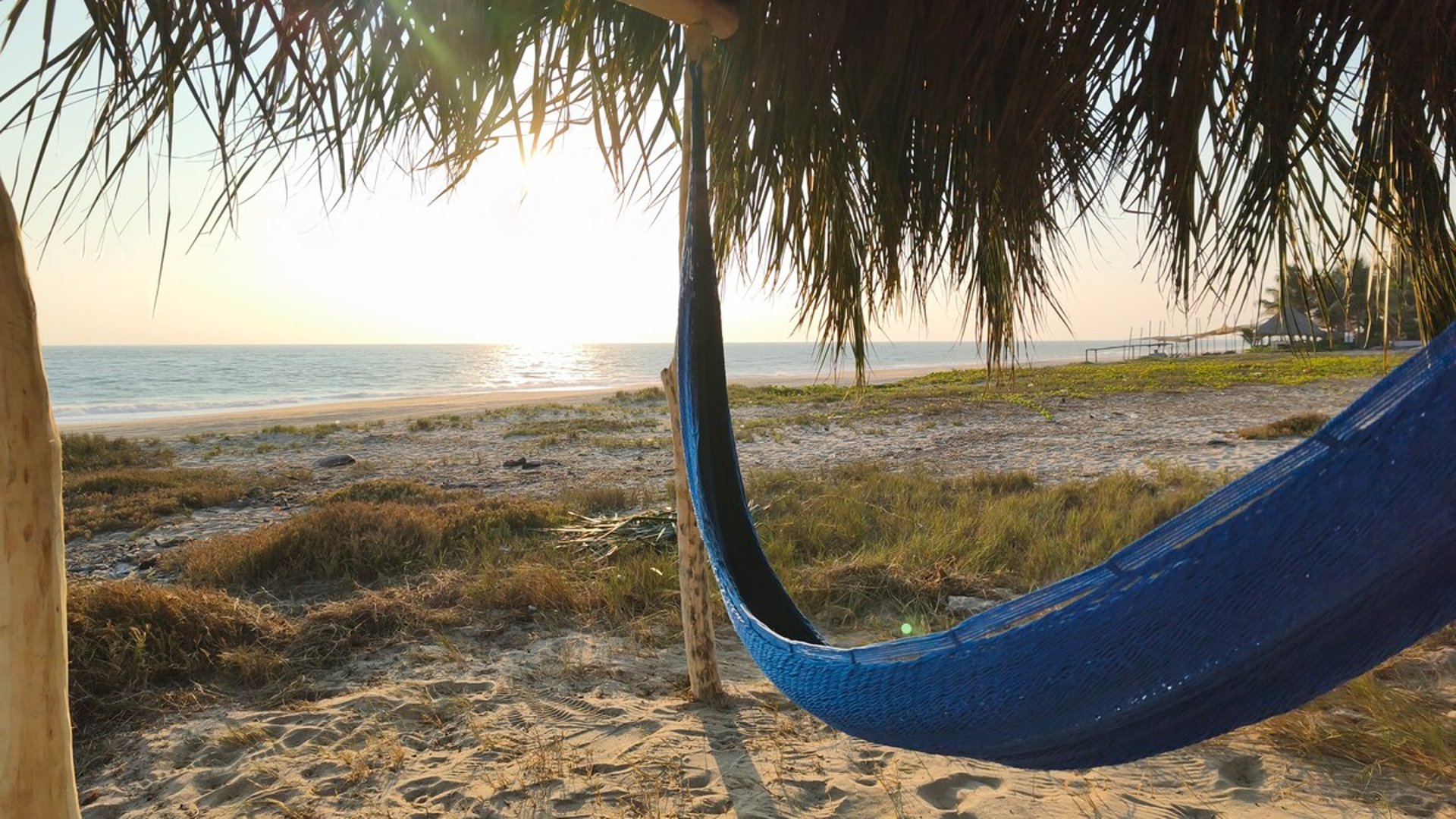 Hamaca azul bajo palapa frente al mar con luz dorada del atardecer en la playa