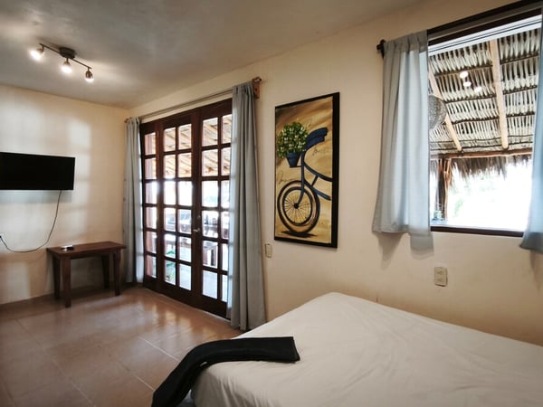 Recámara amplia con cama doble, TV, puertas francesas y ventana con vista a palapa exterior