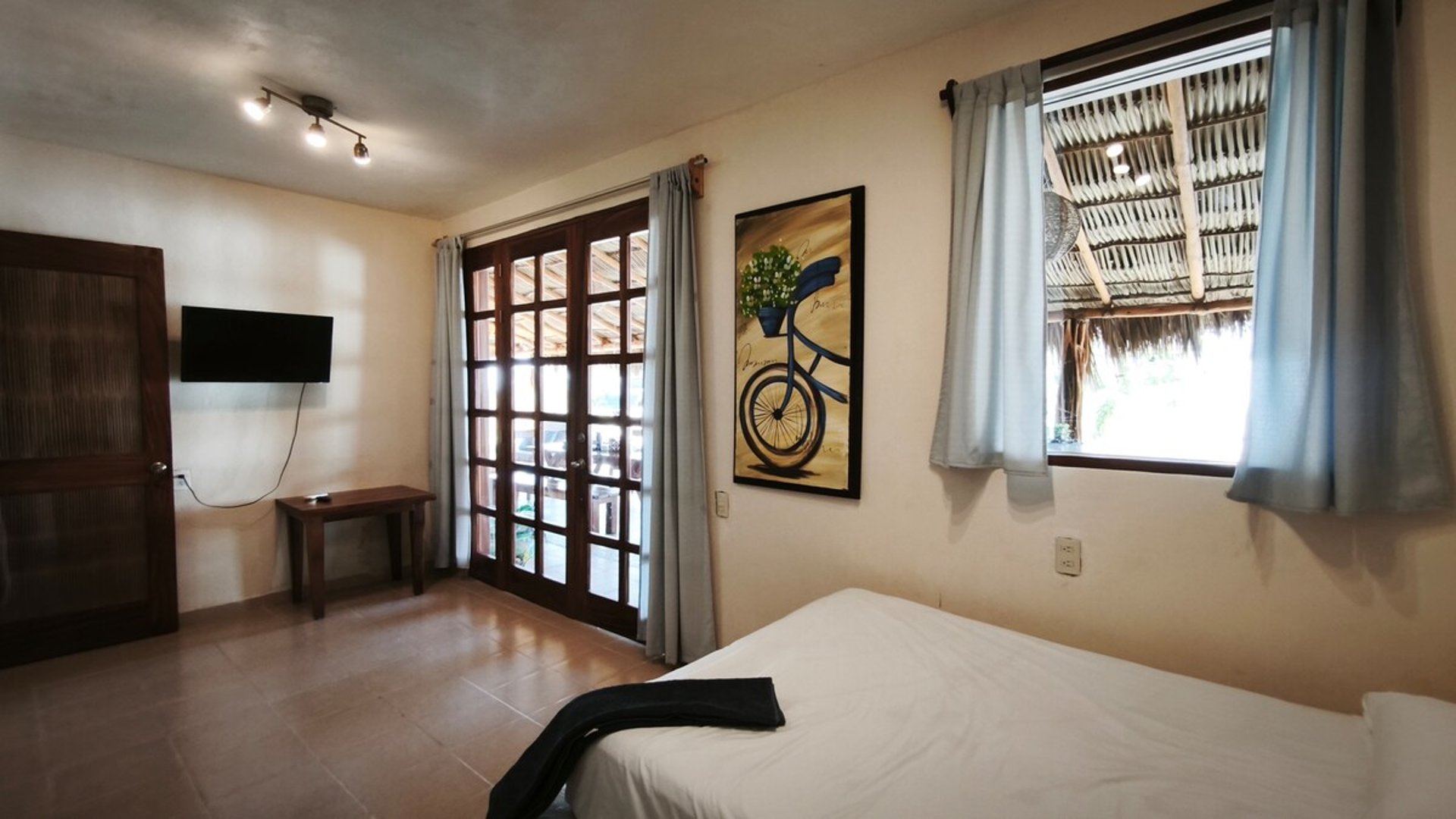 Recámara amplia con cama doble, TV, puertas francesas y ventana con vista a palapa exterior