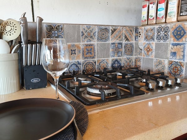 Estufa de gas de cinco quemadores con salpicadera de talavera colorida, utensilios y copa de vino sobre la barra