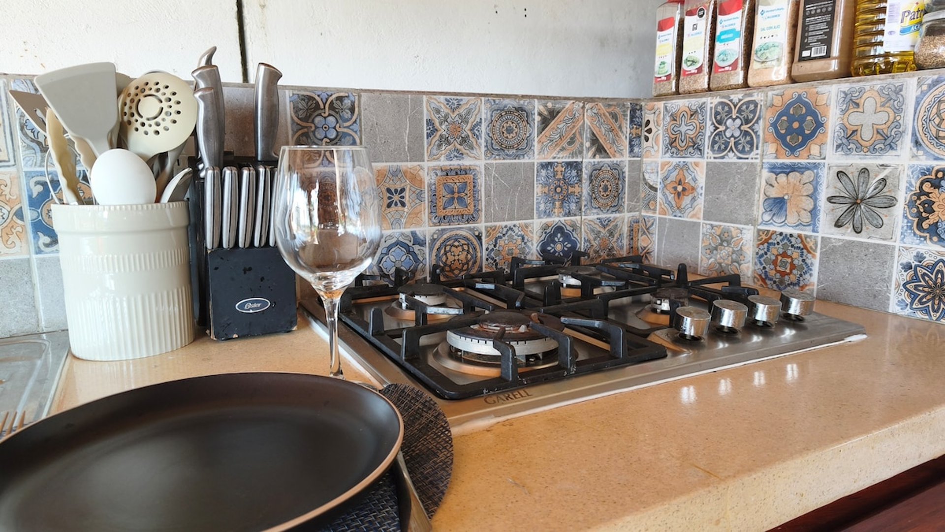 Estufa de gas de cinco quemadores con salpicadera de talavera colorida, utensilios y copa de vino sobre la barra