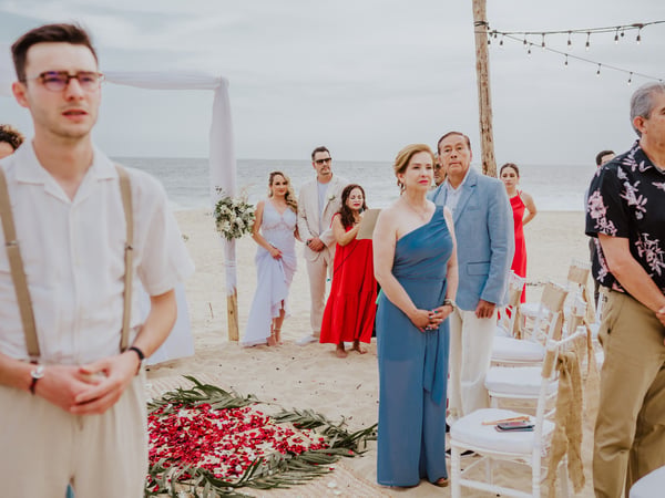Ceremonia de boda en playa con pasillo floral de pétalos rojos y invitados bajo luces colgantes