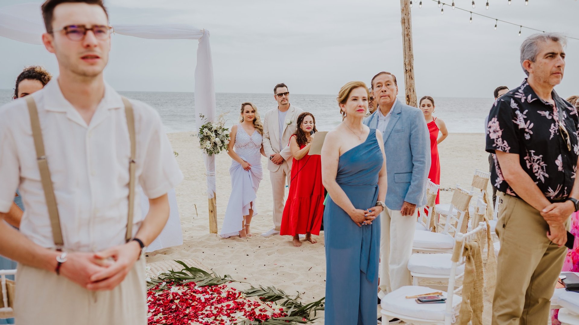 Ceremonia de boda en playa con pasillo floral de pétalos rojos y invitados bajo luces colgantes