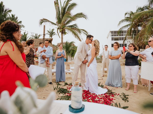 Ceremonia de boda en villa frente al mar con palmeras y pétalos rojos en pasillo de arena