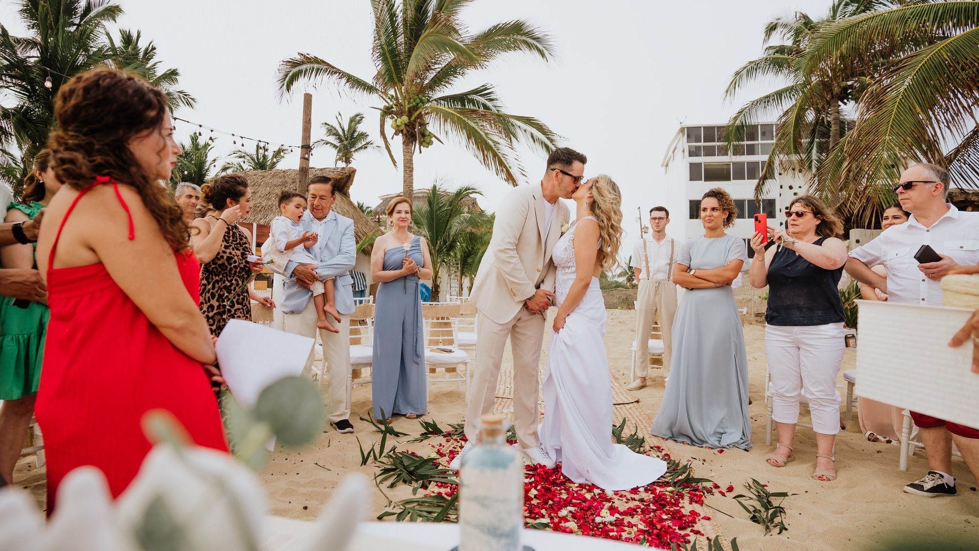 Ceremonia de boda en villa frente al mar con palmeras y pétalos rojos en pasillo de arena