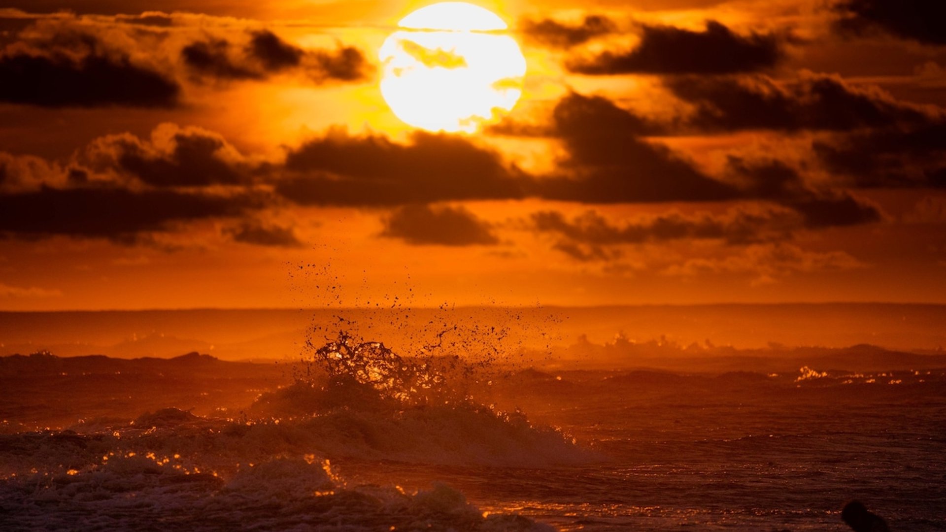 Atardecer intenso sobre el Pacífico con olas rompiendo en silueta bajo un sol ardiente entre nubes dramáticas