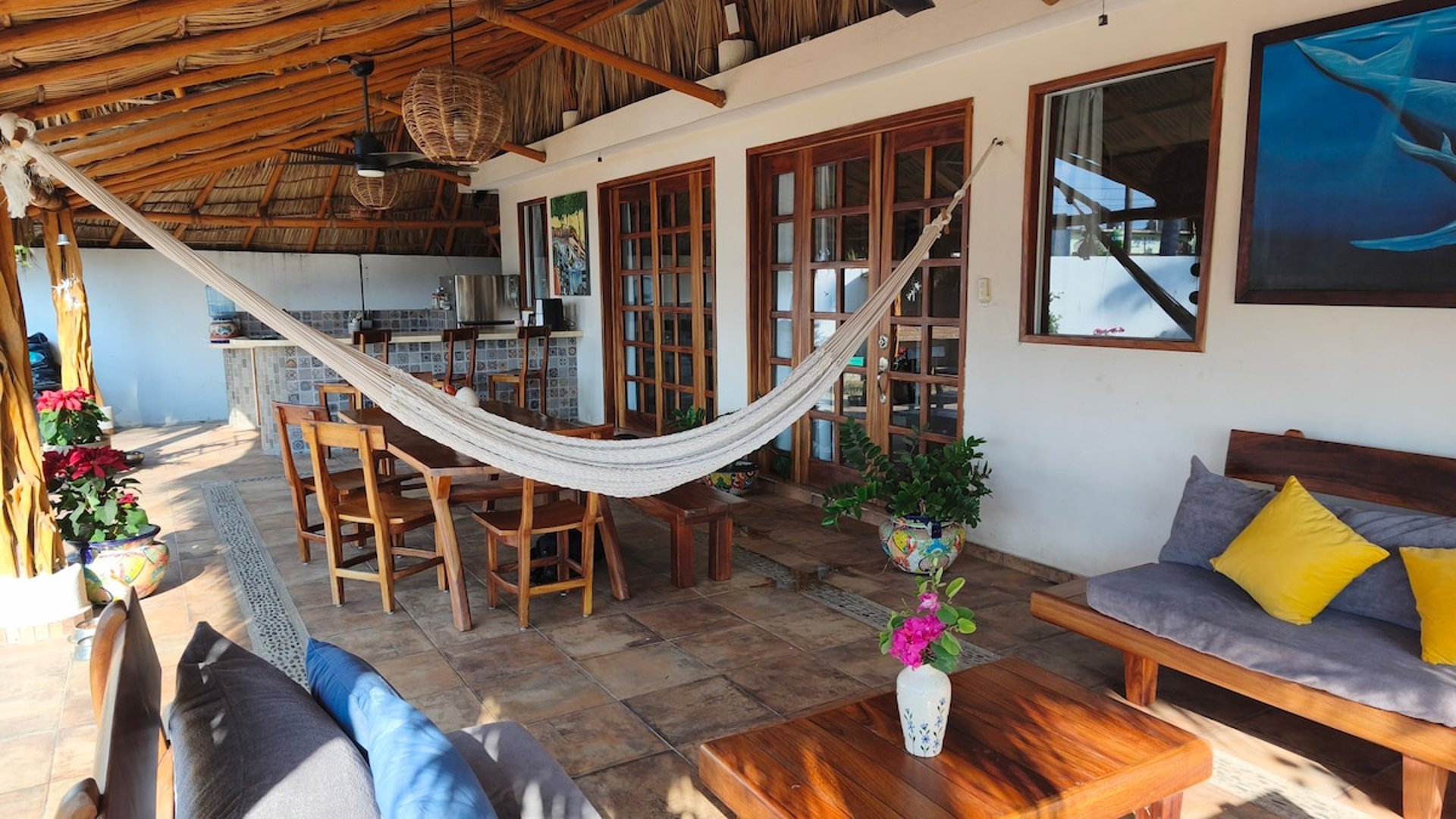 Terraza bajo palapa con hamaca, sala y comedor exterior rodeados de decoración artesanal mexicana