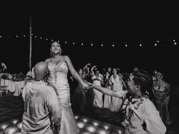 Fiesta de boda nocturna en playa con luces colgantes y invitados celebrando en pista