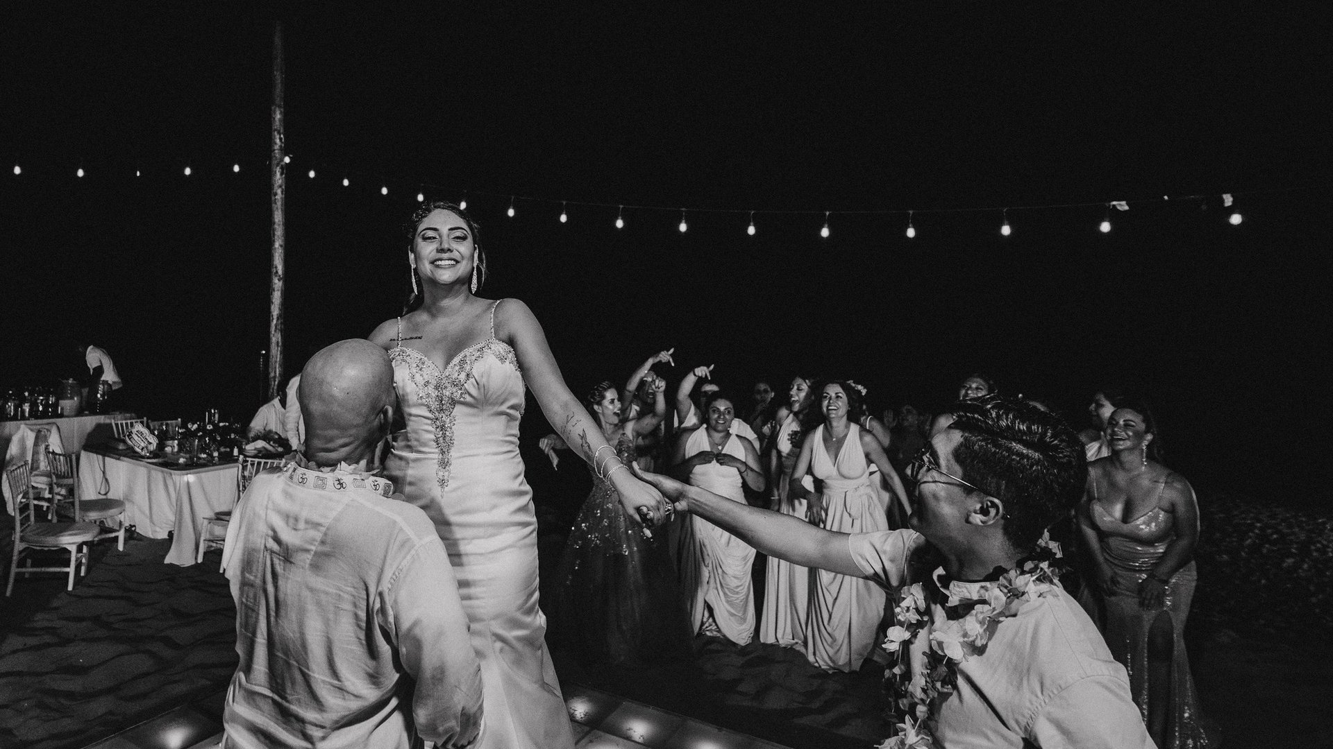 Fiesta de boda nocturna en playa con luces colgantes y invitados celebrando en pista