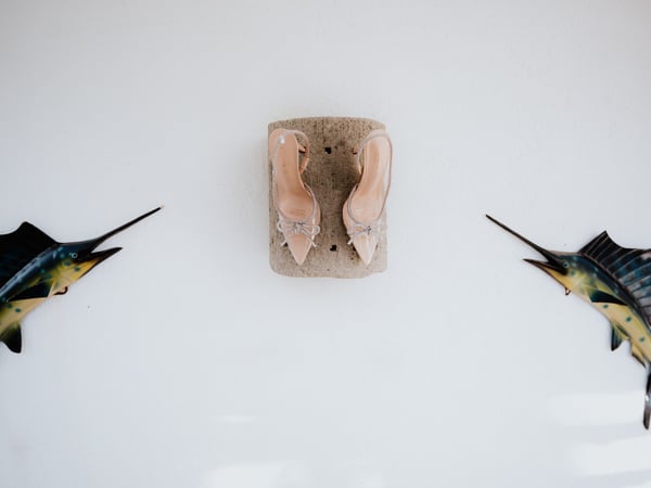 Zapatos de novia sobre piedra coral con decoración de peces vela en pared blanca de villa costera