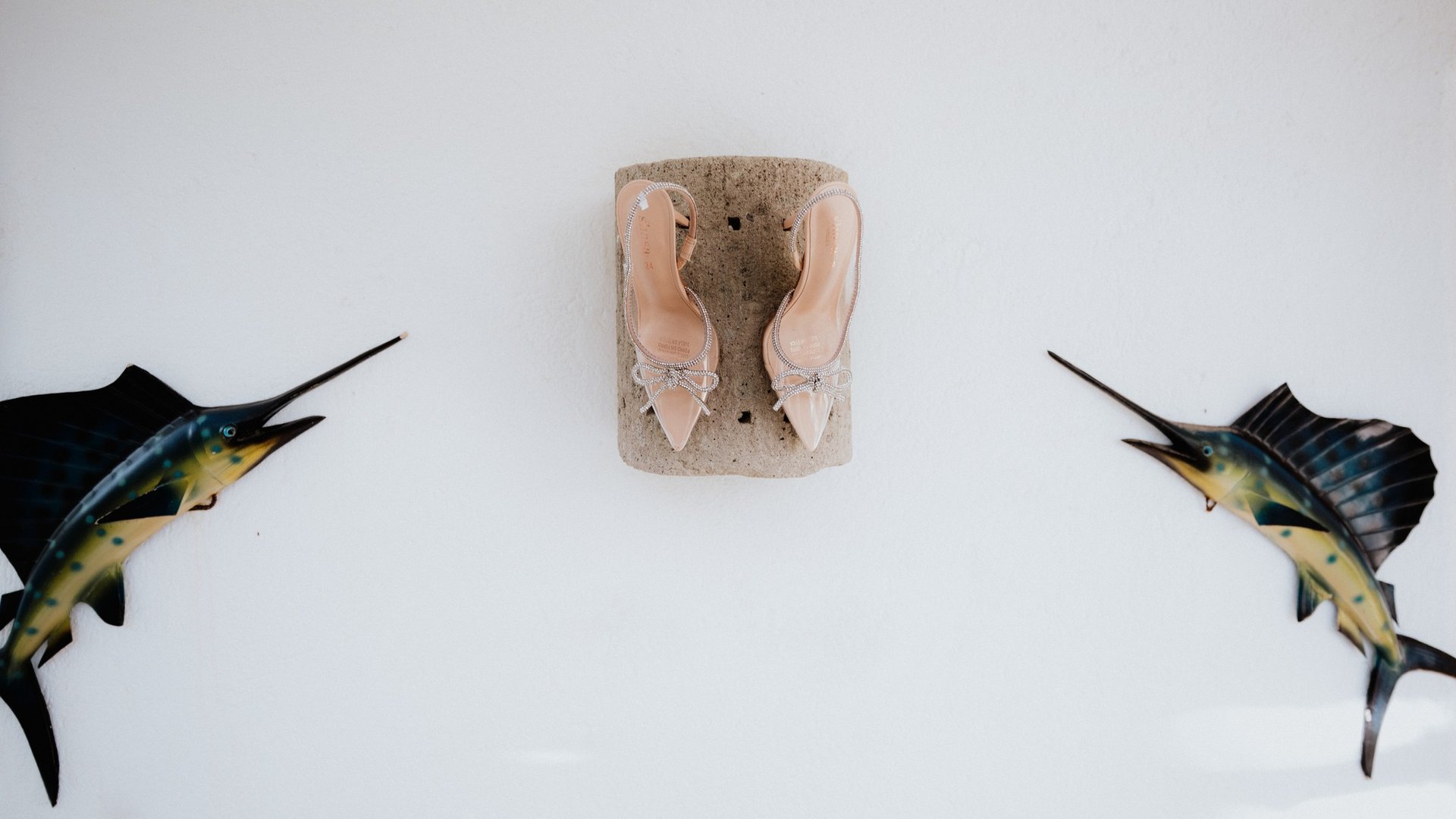 Zapatos de novia sobre piedra coral con decoración de peces vela en pared blanca de villa costera