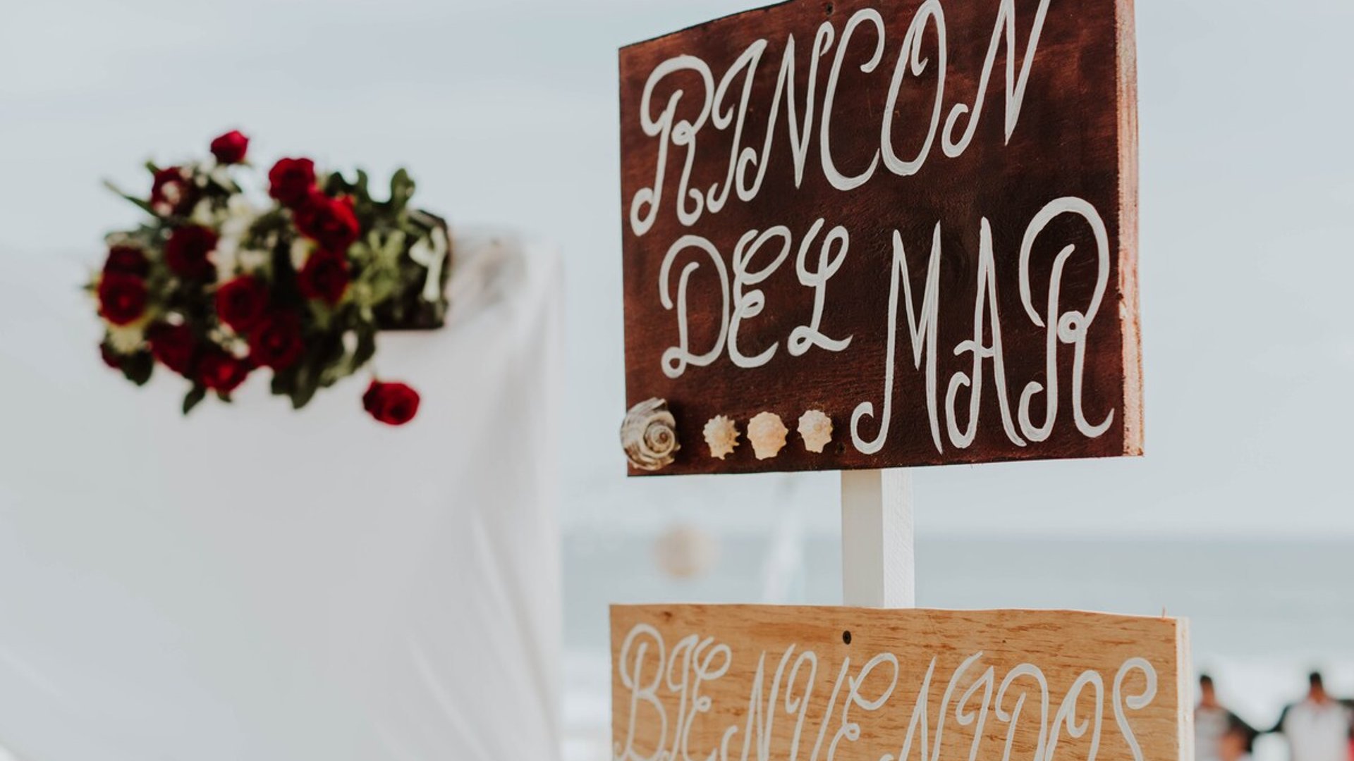 Letrero de bienvenida de Rincón del Mar con decoración floral de rosas rojas y vista al mar de fondo