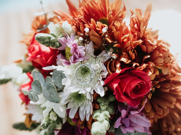 Ramo de novia con flores tropicales naranjas, rosas rojas y eucalipto con anillos de boda
