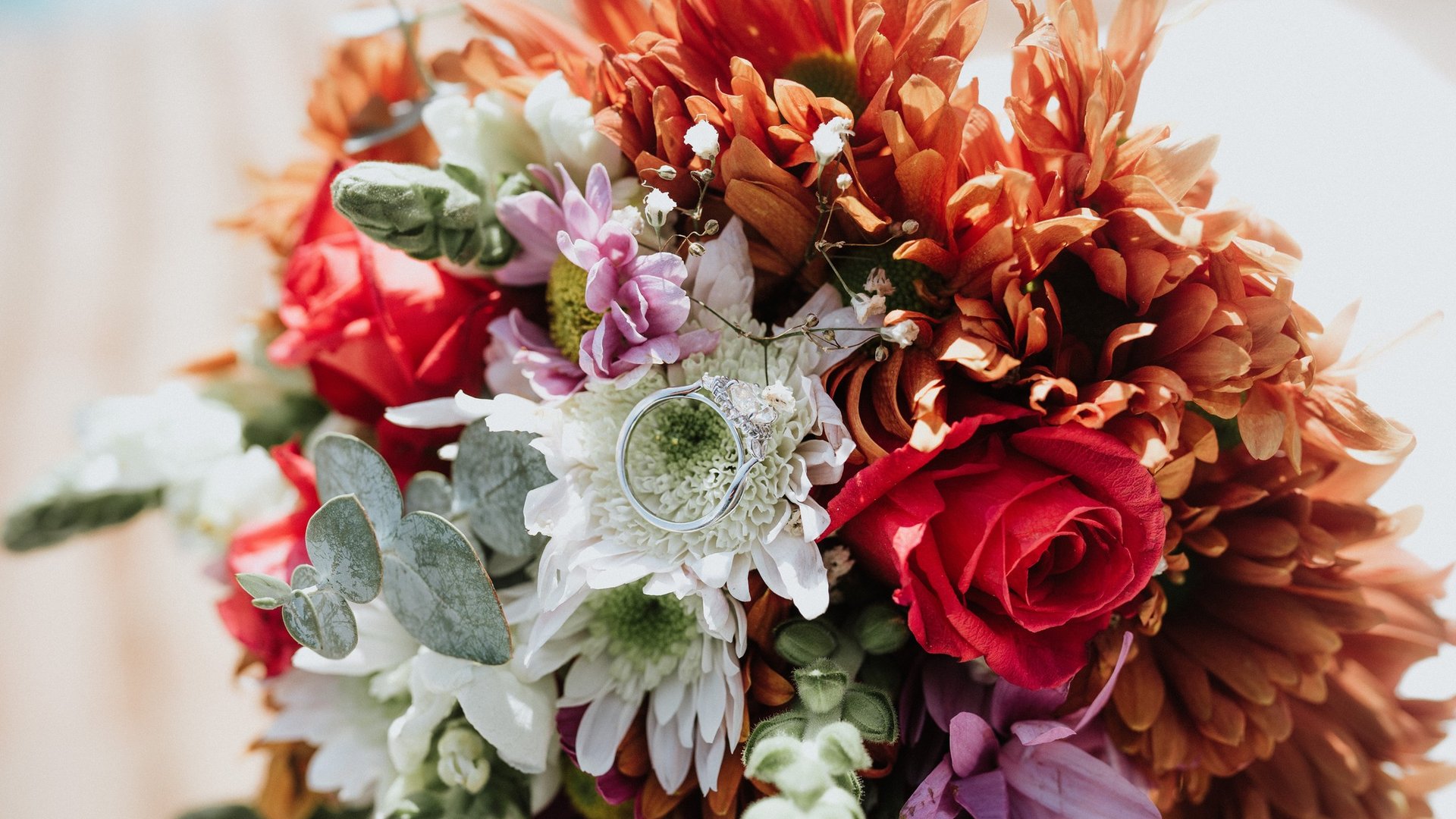 Ramo de novia con flores tropicales naranjas, rosas rojas y eucalipto con anillos de boda