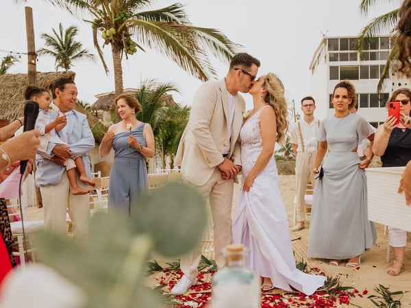 Ceremonia de boda frente a villa playera con palmeras y pasillo de pétalos rojos