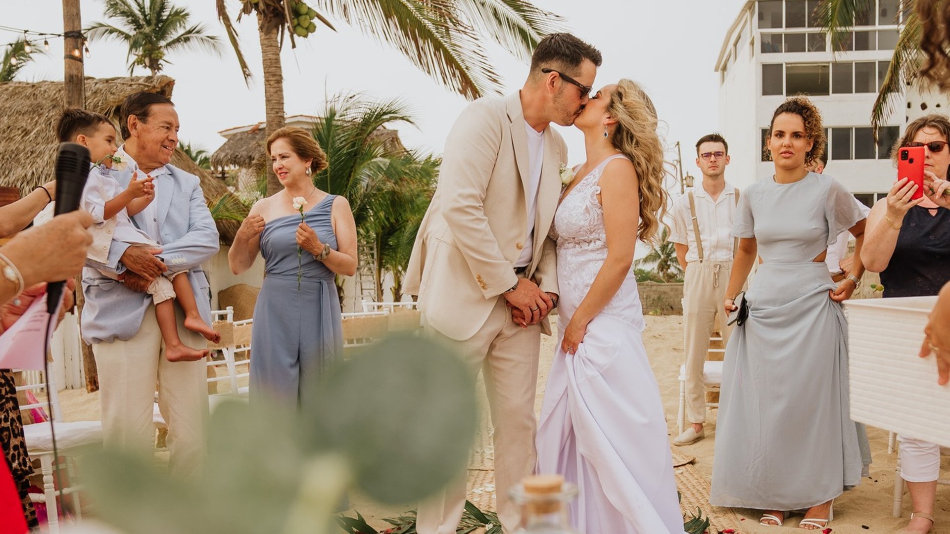 Ceremonia de boda frente a villa playera con palmeras y pasillo de pétalos rojos