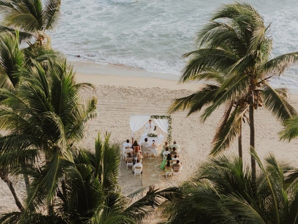 Ceremonia de boda íntima en la playa entre palmeras tropicales, con altar blanco frente al mar turquesa