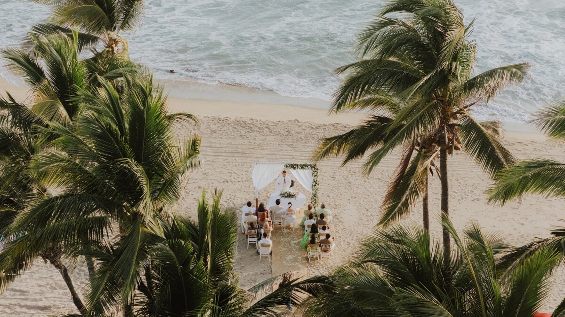 Ceremonia de boda íntima en la playa entre palmeras tropicales, con altar blanco frente al mar turquesa