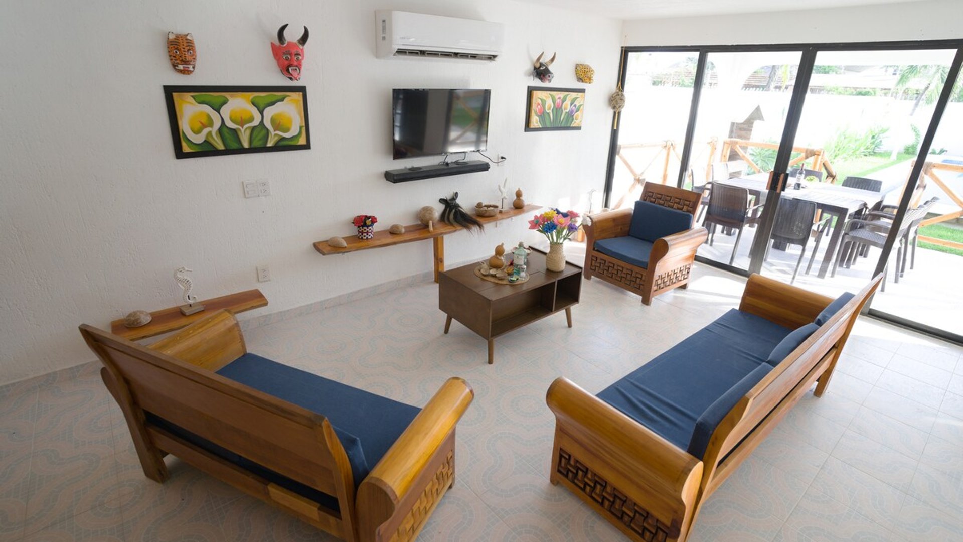 Sala amplia con muebles de madera y cojines azules, decoración artesanal mexicana y acceso directo a terraza exterior