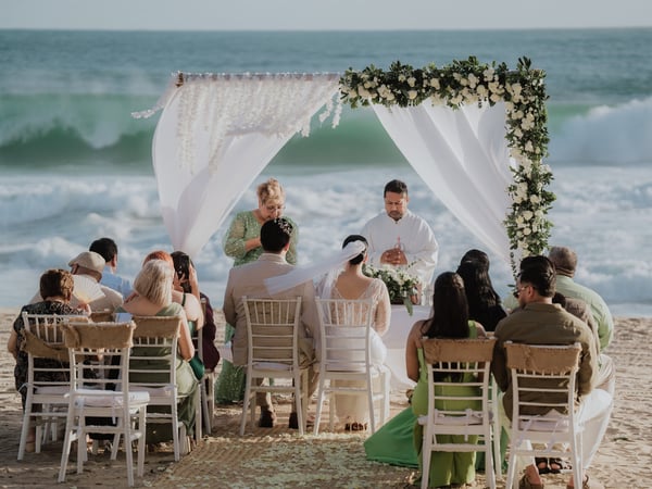 Ceremonia de boda en playa con arco floral blanco frente al mar Pacífico y sillas tiffany