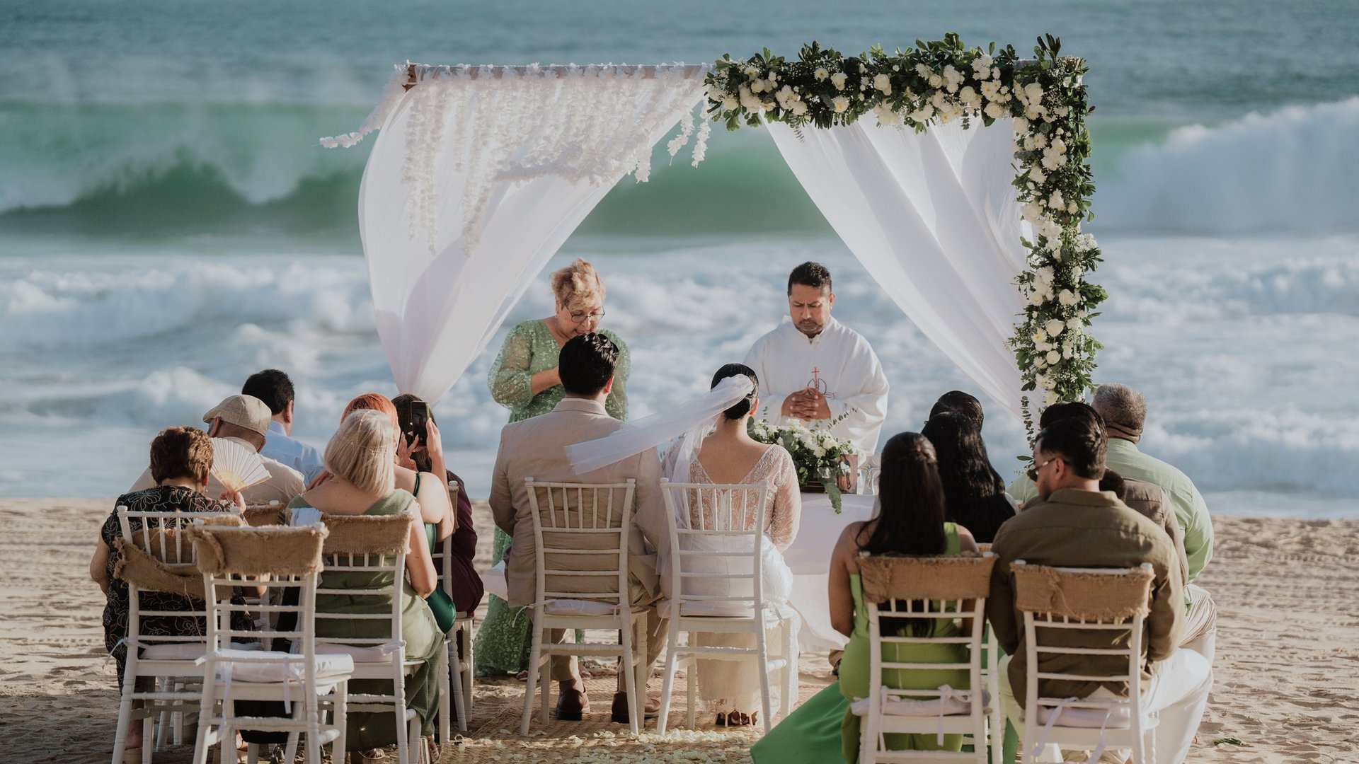 Ceremonia de boda en playa con arco floral blanco frente al mar Pacífico y sillas tiffany
