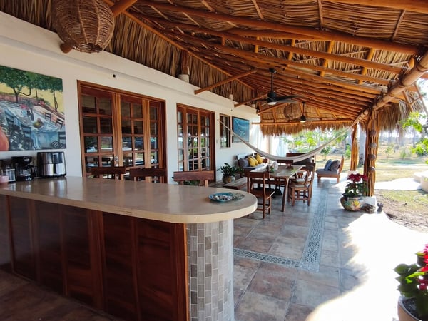 Terraza palapa con barra de mosaico, comedor exterior, hamaca y sala al aire libre bajo techo de palma