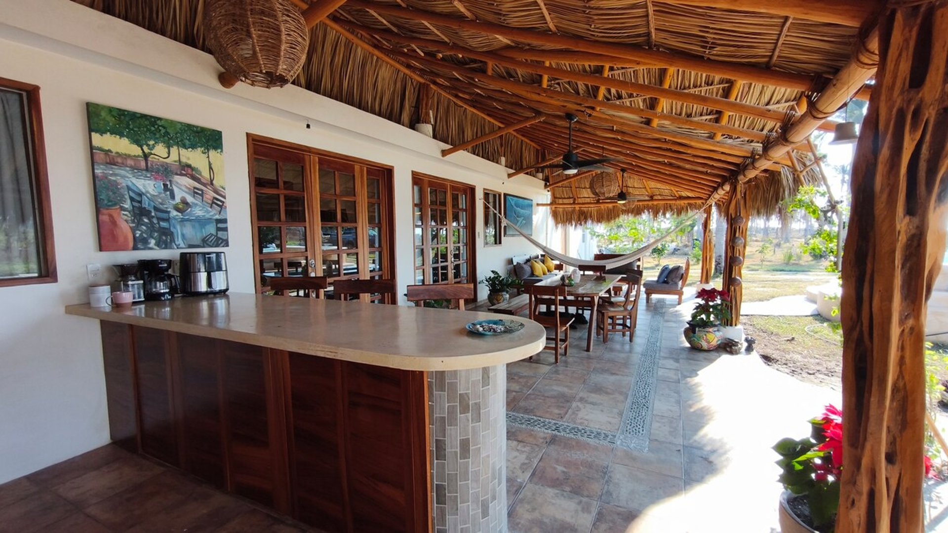 Terraza palapa con barra de mosaico, comedor exterior, hamaca y sala al aire libre bajo techo de palma